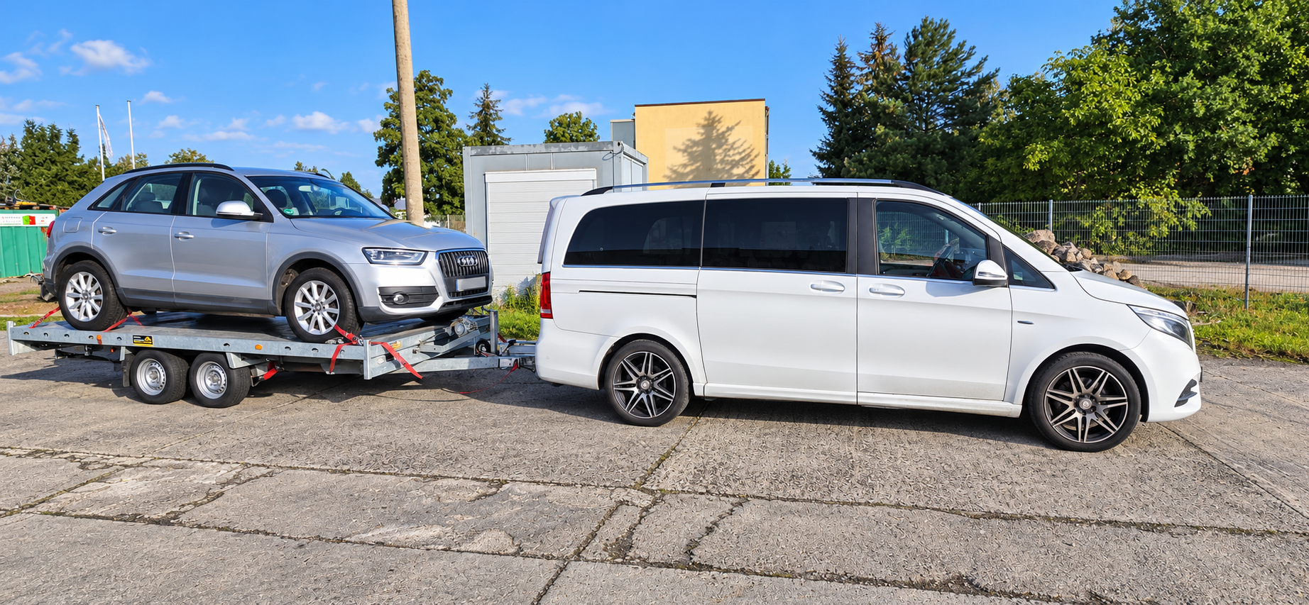 Weißer Transporter mit einem silbernen Pkw auf dem Autotransportanhänger